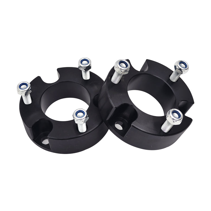 A pair of black, round coil spring spacers or strut spacers for a vehicle lift kit. They are solid rings with cutouts and bolt holes, and each spacer has three silver bolts with washers and blue-ringed nuts attached to it. They are likely made of aluminum or a similar durable material.