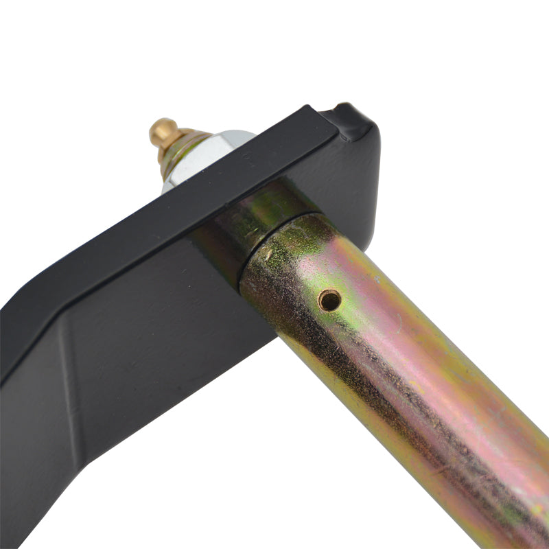 A close-up shot focusing on the connection point of a black metal suspension shackle plate and a gold-colored metal bolt/bushing. The bolt is inserted through the hole in the plate. The end of the bolt is secured with a silver nut and features a small brass zerk fitting (grease nipple) on top for lubrication. A small lubrication hole is visible on the side of the gold-colored bolt/bushing. The background is white.