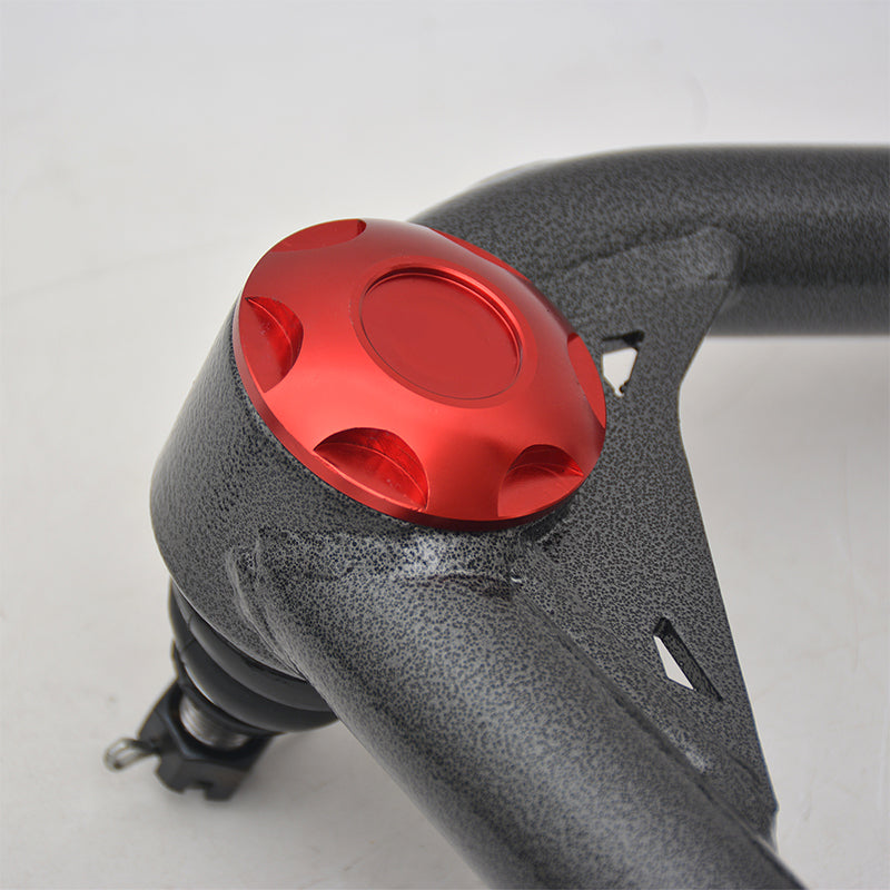 Close-up of a high-performance, aftermarket upper control arm (UCA) for a vehicle's suspension, featuring a dark gray hammertone finish. A prominent, bright red, circular aluminum dust cap with a scalloped edge and a central recessed circle is bolted onto the ball joint housing.