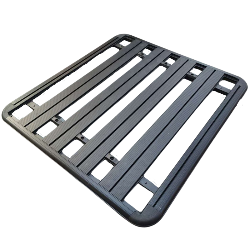 A close-up, high-angle studio shot of a black, heavy-duty aluminum platform roof rack for a 4x4 or SUV, isolated against a white background. The rack has rounded corners, a flat perimeter frame, and five thick, lengthwise slats with numerous rectangular openings for mounting accessories.