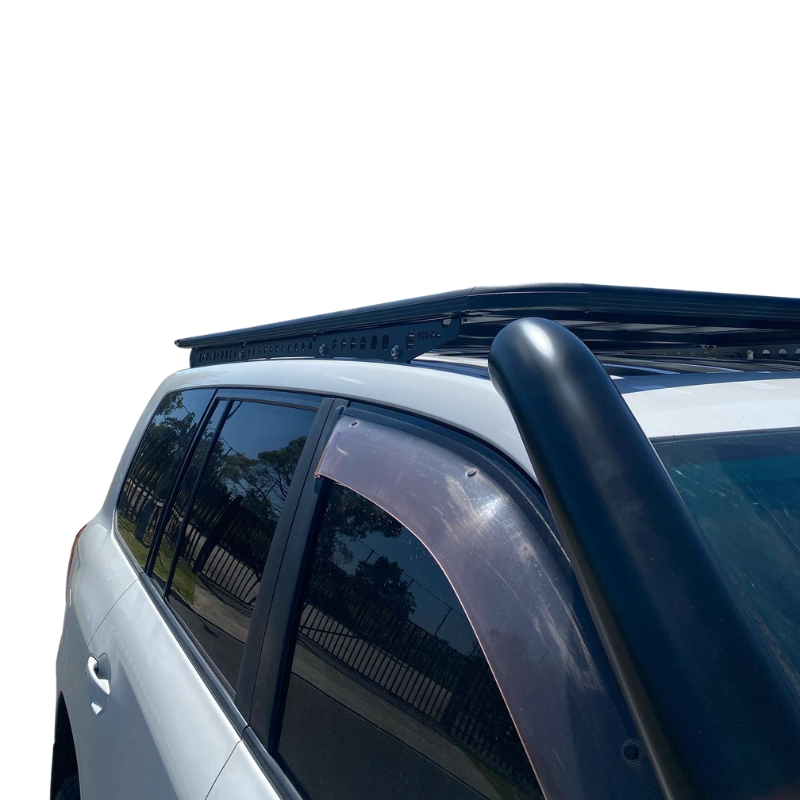 A low-angle shot showing the roof rack and snorkel on a white SUV, likely a four-wheel drive vehicle. The roof rack is a black, flat platform style mounted low to the roof. A large, black air intake snorkel runs up the passenger side A-pillar. Dark-tinted weather shields (wind deflectors) are installed above the side windows. The background is overexposed, making the vehicle accessories the main focus.