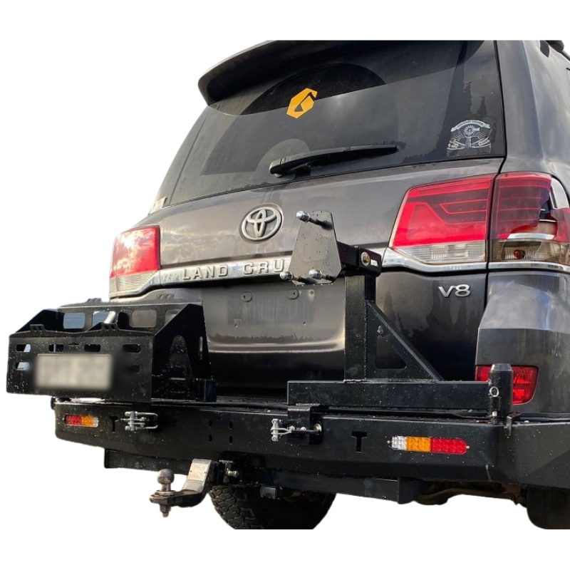 A close-up, rear quarter-view image of a dark gray Toyota Land Cruiser 200 Series SUV, showcasing a heavy-duty, black steel rear bar with dual swing-out carriers installed.
The image focuses on the carriers in their open position:
The left swing-out carrier is a large, rectangular storage box with multiple compartments, seen swinging open to the left.
The right swing-out carrier is a spare tire mounting post with a plate, seen swinging open to the right.