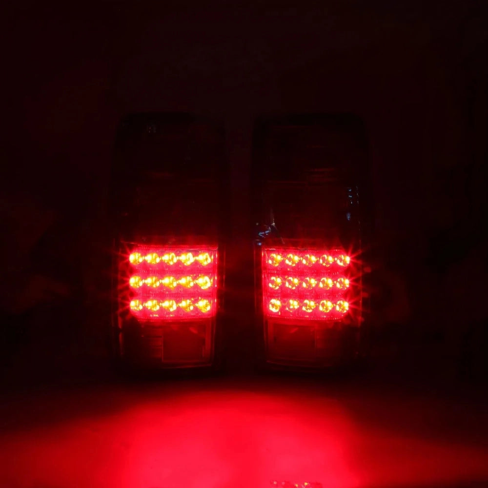 A low-light image showing a pair of red LED taillight assemblies illuminated. The central section of each light contains a bright matrix of approximately three rows of round, red LEDs that are glowing intensely, casting a strong red light in the surrounding darkness.