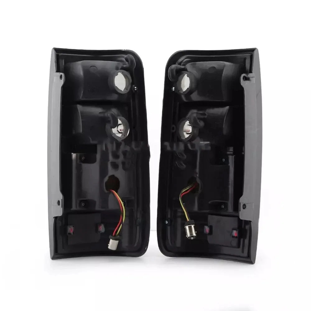 A pair of matching black vehicle taillight assemblies shown from the back, displaying the bulb socket openings and wiring harnesses. Each assembly has two large upper openings and a lower opening with a small bulb socket and attached red, black, and yellow wires visible, confirming they are a left and right set.