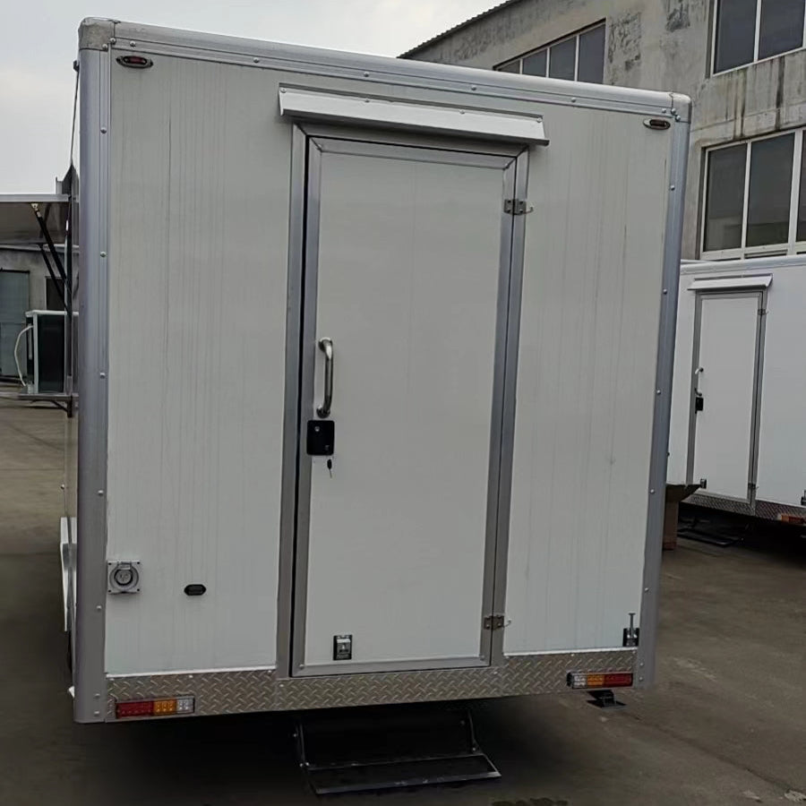 A vertical photo shows the back end of a white, enclosed utility trailer, which appears to be a refrigerated or food service trailer. The back panel features a single white door with a silver handle, lock, and hinges, centered vertically on the trailer. A small, retractable metal step is extended below the door. The bottom edge of the trailer has a strip of diamond plate metal, and below that are taillights and reflectors. The trailer is parked on a gray, concrete or paved lot, with a large, industrial-loo