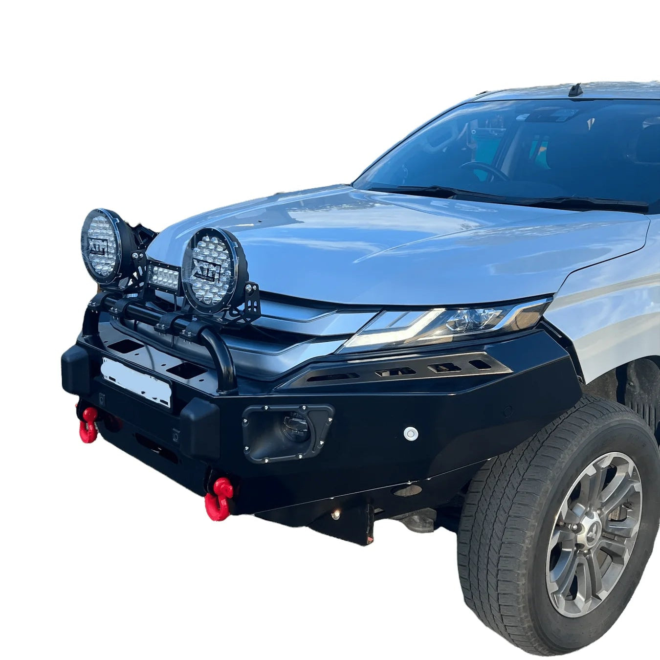 A three-quarter front view of a silver Mitsubishi Triton/L200 pickup truck, showing a heavy-duty, matte black steel bull bar/bumper installed.
The bull bar is equipped with:
A central steel hoop that holds an LED light bar and two large, round LED driving lights (labeled XTM).
Recessed, angled light openings (possibly for fog lights or indicators) integrated into the bumper corners.
Two prominent red recovery shackles mounted underneath the bumper.
A mounting point for a license plate in the center.