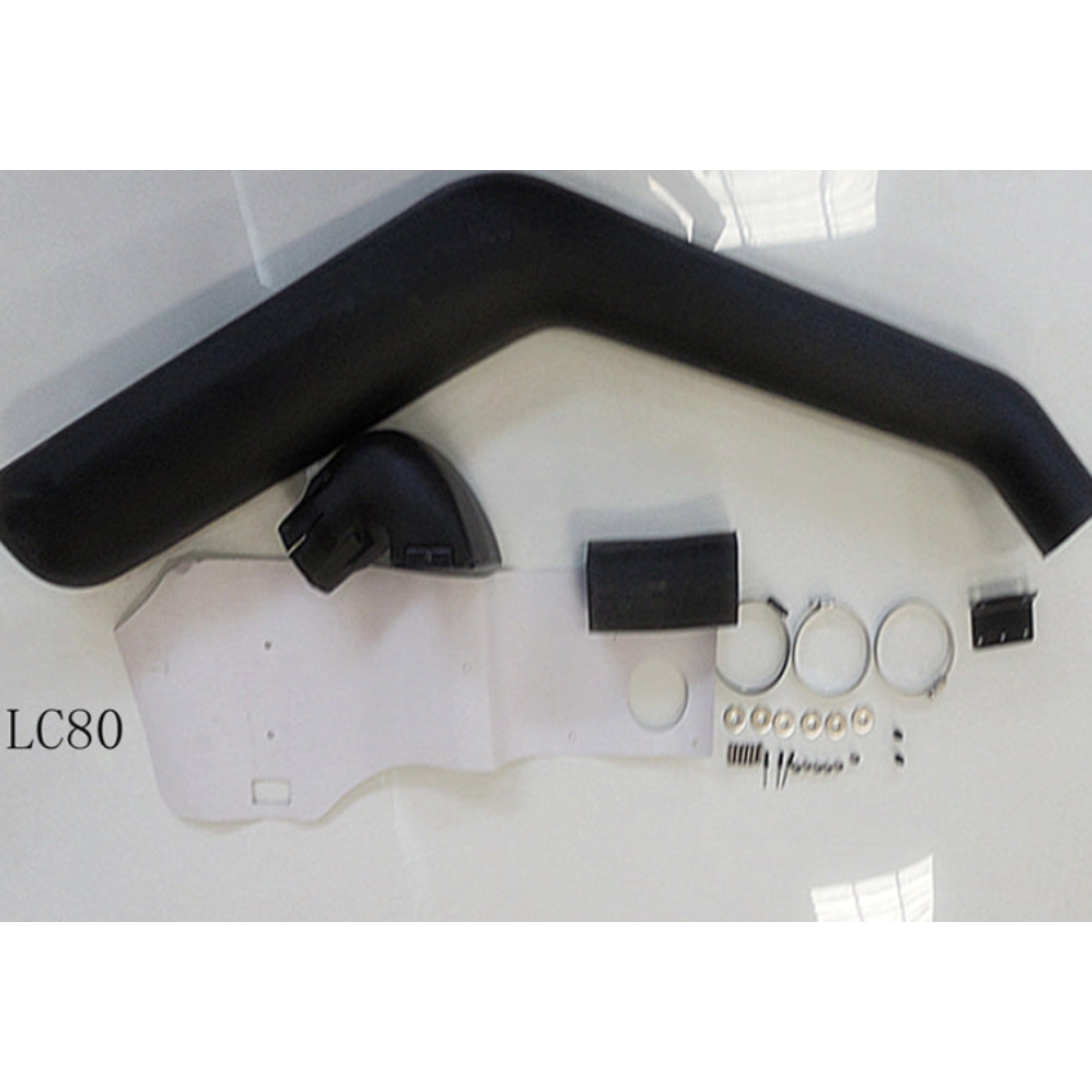 An overhead flat lay of a black automotive snorkel kit for a Toyota Land Cruiser 80 series (labeled LC80 in the lower left corner), displayed against a white background. The kit includes the long, curved main black plastic snorkel pipe, a smaller connecting elbow piece, a large, white paper or plastic template, a black rubber-like piece, a black metal bracket, three metal hose clamps, and a pile of small metal washers and fasteners.