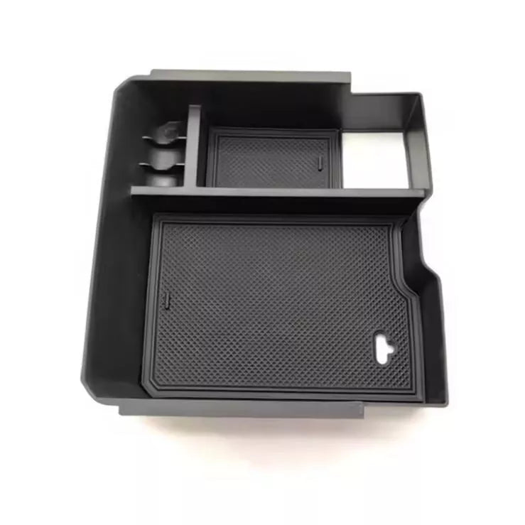A studio product image showing a black plastic center console organizer tray for a vehicle, isolated on a white background. The tray features multiple deep compartments, including a large main section and smaller sections for coins or phones. The two largest compartments contain removable black rubber anti-slip mats with a diamond grid texture.