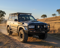 Modified silver Toyota Land Cruiser 80 Series SUV driving on a dirt road through dry, golden grass fields at golden hour.