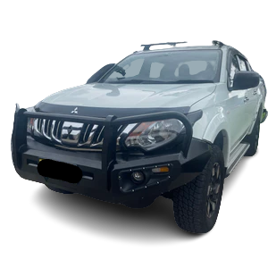 A front-quarter view of a white pickup truck, likely a Mitsubishi Triton, fitted with a substantial black steel bull bar/bumper replacement. The bull bar wraps around the front, protecting the grille and headlights, and has integrated driving lights/fog lights and indicators. The vehicle is set against a checkered, transparent background.