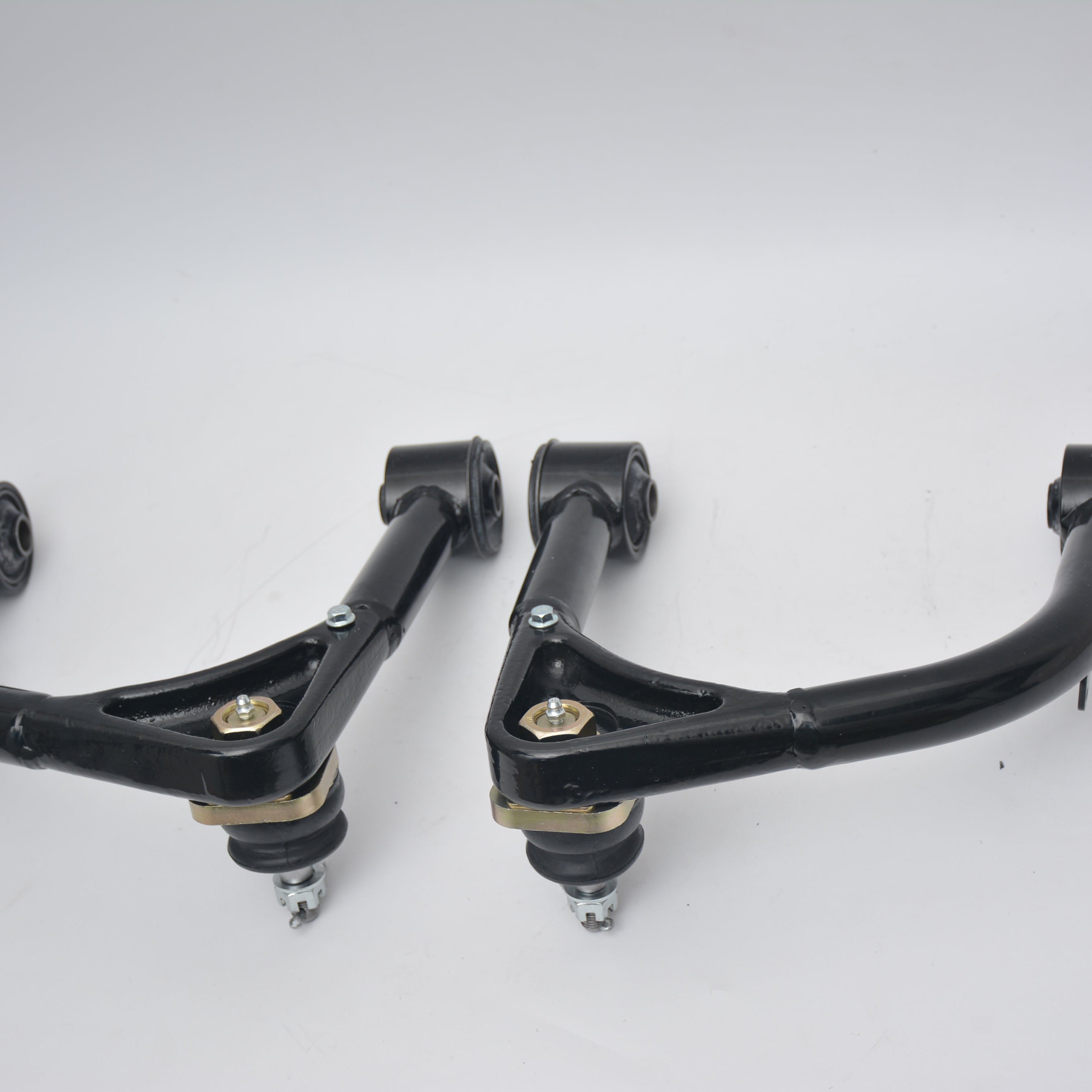 Two fabricated UCAs featuring installed ball joints secured with castle nuts, and inner mounting points fitted with rubber bushings.