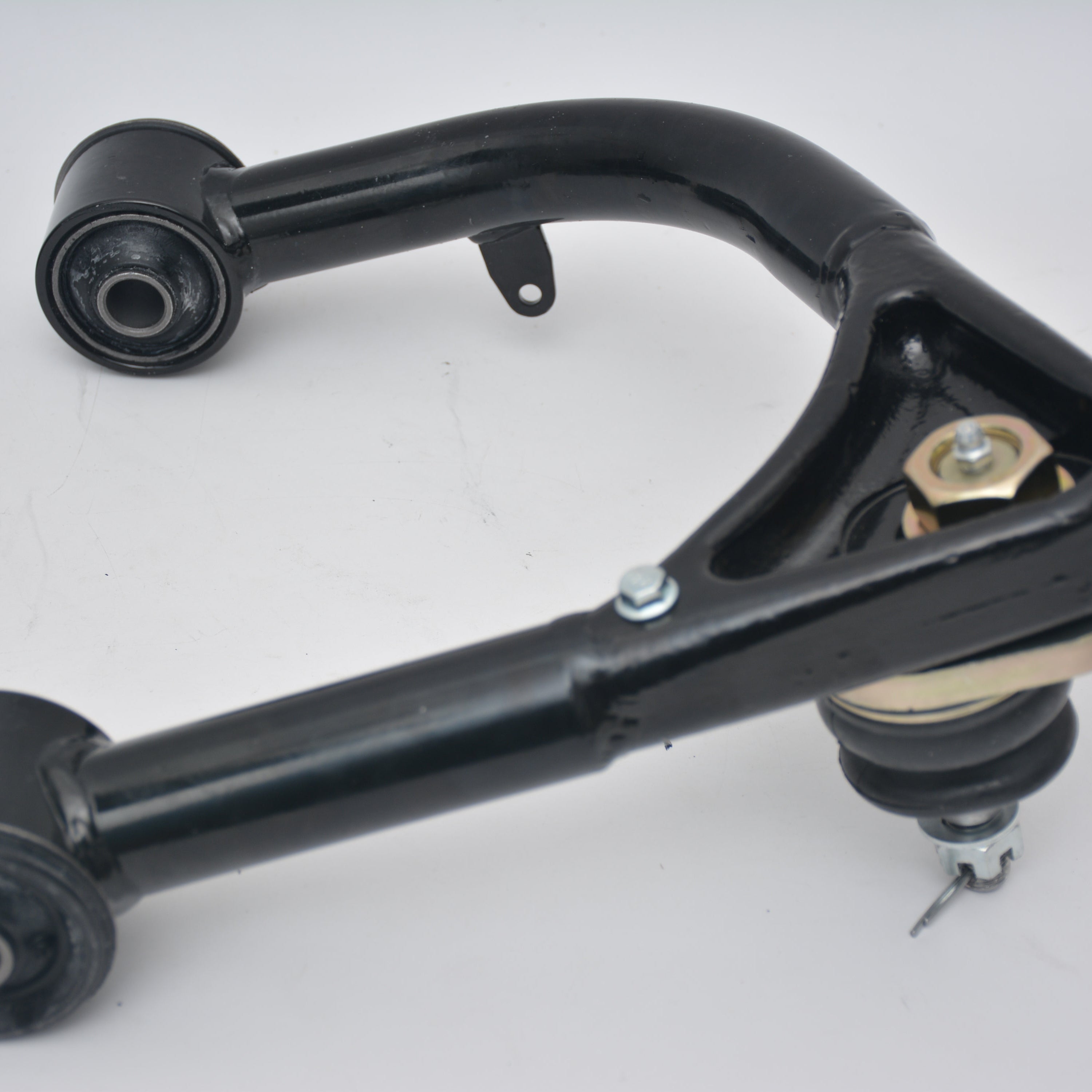 A single, black automotive upper control arm (UCA) is shown against a white background. The arm is a curved, fabricated steel component with a pre-installed ball joint at the spindle connection end, secured by a large gold-colored nut. The opposite end features a rubber bushing for mounting to the frame.