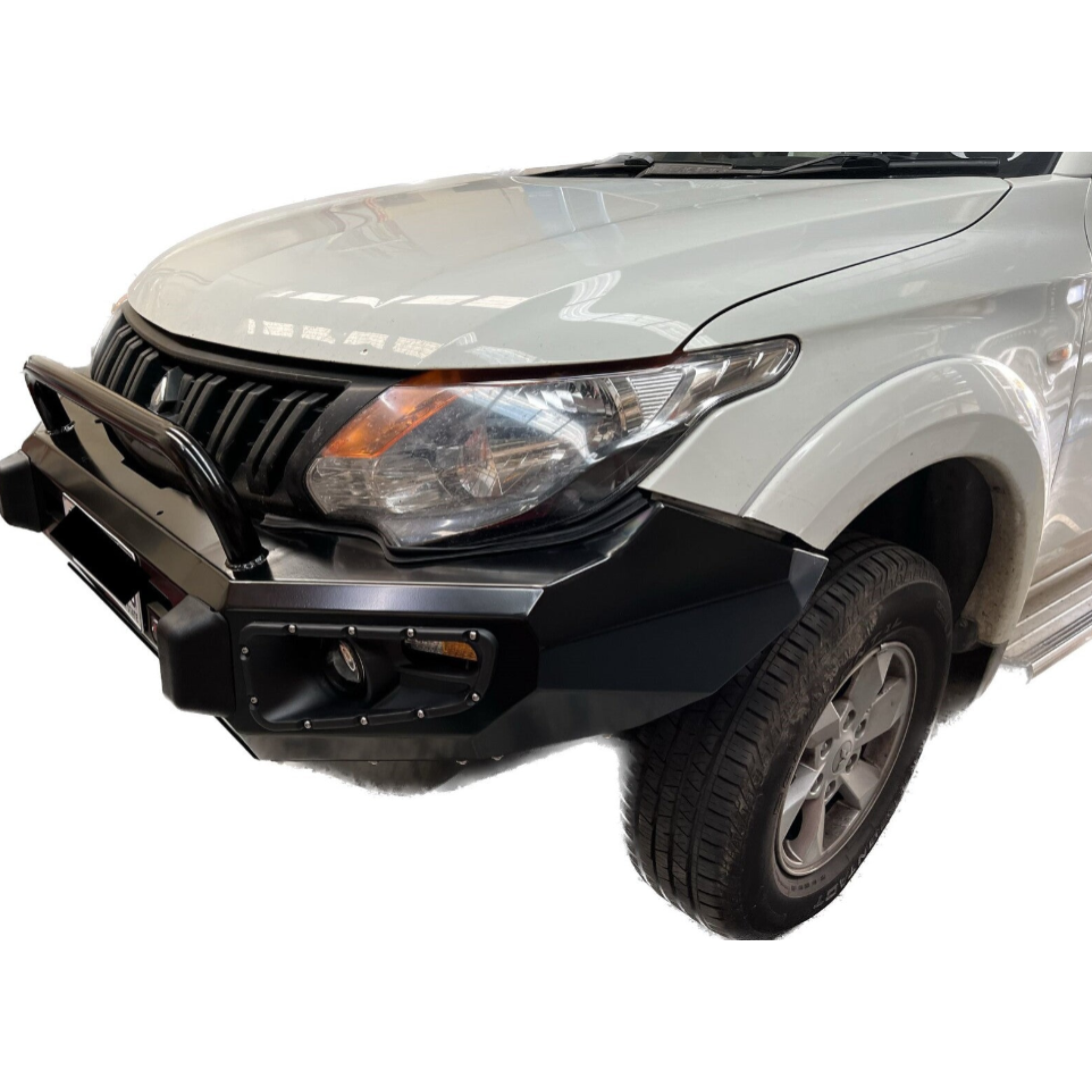 A close-up, three-quarter front view of a white pickup truck, likely an older model Mitsubishi Triton/L200, fitted with a heavy-duty, black steel bull bar/bumper.

The aftermarket bumper features:

A single steel hoop extending in front of the grille.

An angular, aggressive design with a cluster of integrated lights (fog light and indicator) on the corner, surrounded by decorative bolts.

The bumper wraps around the lower section of the white fender flare.

The truck's large original headlight assembly an