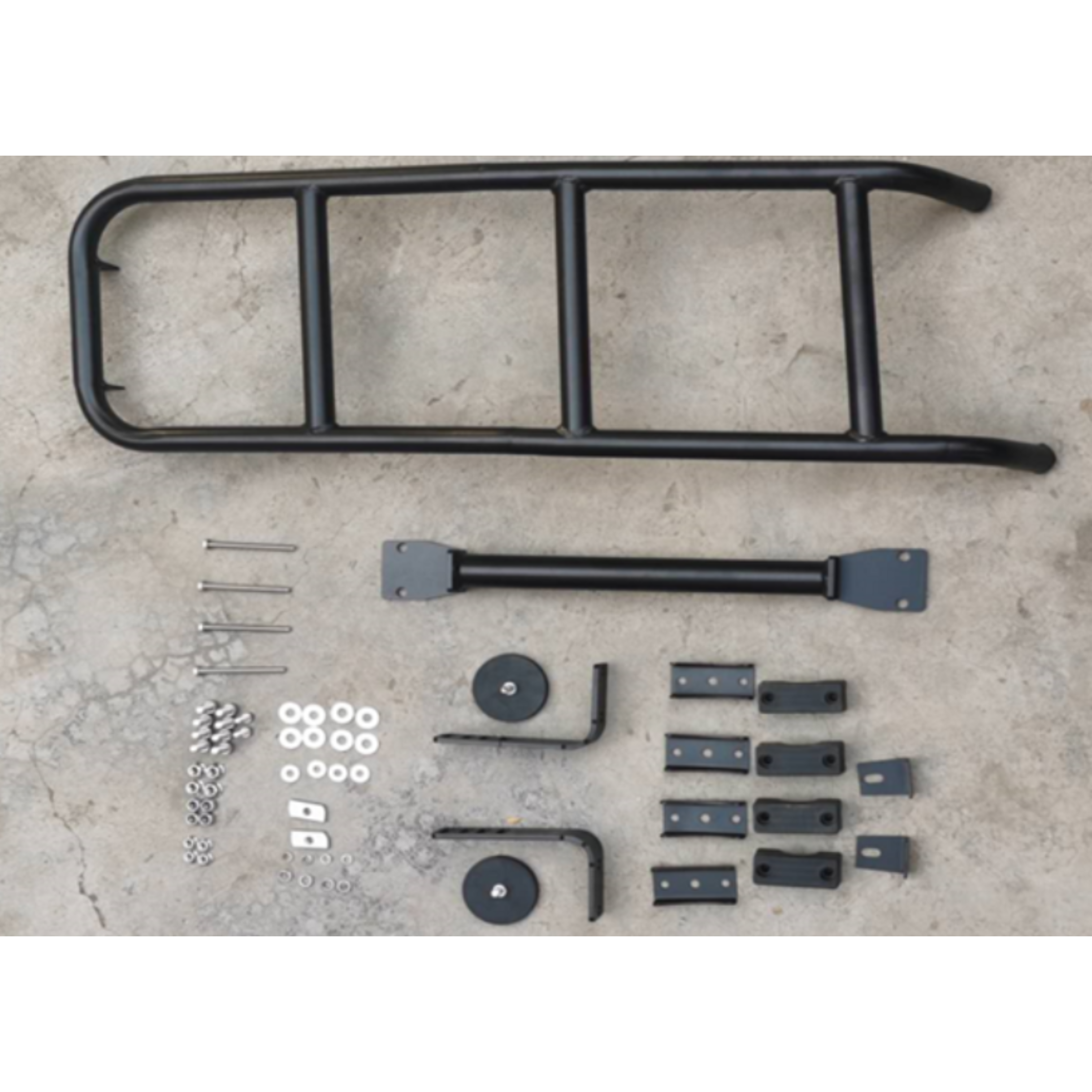 Disassembled black metal ladder kit, likely for the rear of an SUV or 4x4, laid out on a concrete or paved surface. Components include the main tubular ladder frame, a horizontal support bar, various mounting brackets (some with rubber pads), stainless steel bolts, nuts, and washers.