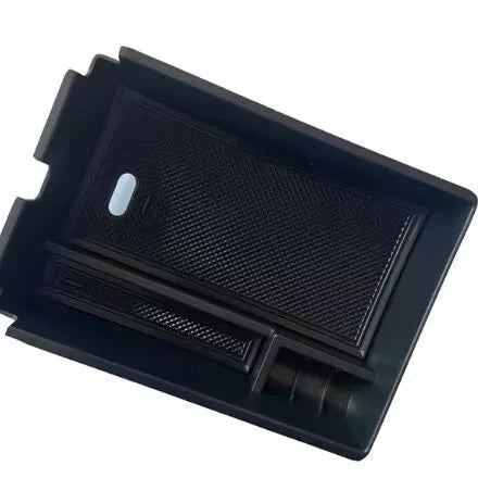 A rectangular black plastic car console organizer tray insert, seen from an angle. The tray features a slightly elevated section on the left and a larger, lower section on the right, creating multiple compartments. Both sections have a textured, non-slip rubber mat insert, which appears to be a separate, removable piece. A small, oval-shaped light or indicator is visible in the upper-left area of the larger mat. This accessory is designed to fit inside an existing car storage area, likely a center console.