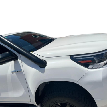 
A close-up view of the front driver's side of a white Toyota Hilux pickup truck, showing the installation of a black automotive snorkel. The base of the snorkel is mounted on the fender near the windshield, and the black intake pipe curves upward along the A-pillar. The vehicle features a black headlight housing and part of a knobby tire is visible at the bottom.