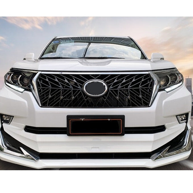A head-on view of the front of a white SUV, likely a Toyota Land Cruiser Prado, that has been customized. The vehicle features an aftermarket black grille with a geometric spoke pattern and a blank oval center where a badge would typically be. The grille is flanked by custom headlights with LED accents and a modified, aggressive-looking white front bumper with chrome trim pieces.