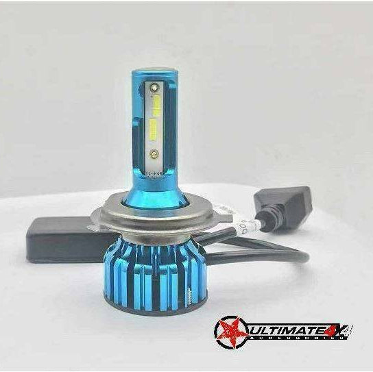 A close-up product photograph of a single LED headlight bulb, featuring a blue anodized aluminum heat sink with cooling fins on the lower section and an upper section housing the white LED chips. A small black connector and wiring are visible, and the image includes the "ULTIMATE 4X4 ACCESSORIES" logo with a red star in the bottom right corner.