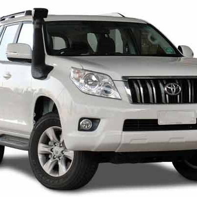 
An eye-level close-up of the front quarter of a white Toyota Land Cruiser Prado SUV with a black snorkel mounted on the driver's side A-pillar and fender. The snorkel extends up the side of the windshield. The vehicle appears to be an off-road model, possibly modified for water crossings or dusty environments.