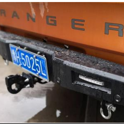 A close-up rear view of an orange Ford Ranger pickup truck with an aftermarket, heavy-duty, matte black steel rear bumper installed, showing water droplets on the surface.

The bumper features:

An integrated horizontal LED light on the right side.

A tow hitch receiver on the left with a heavy-duty, curved tow hook attached.

A D-ring shackle mounted on the bottom right.

A blue license plate mounted on the left side of the bumper.
