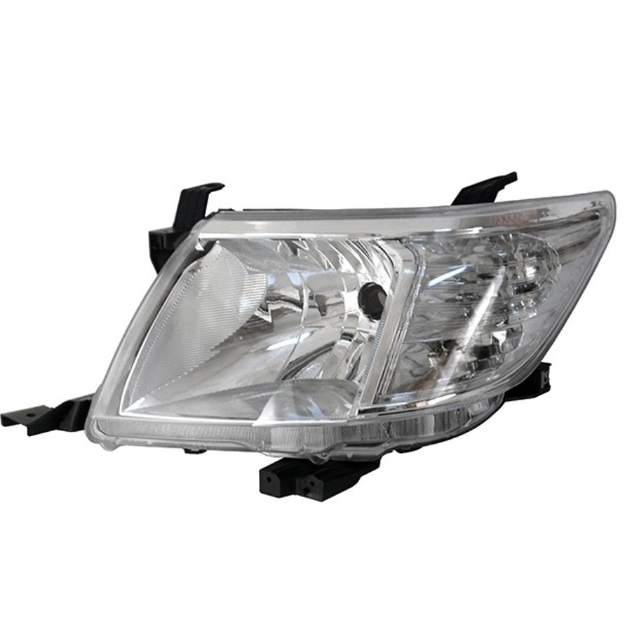 A clear, close-up photograph of a single automotive headlight assembly. The housing is made of transparent plastic, revealing the reflectors and bulb area inside. It has a slightly tapered, rectangular shape with mounting brackets visible on the top and bottom. The design suggests it is for a truck or SUV, possibly a Toyota Hilux (based on the shape). The background is plain white.