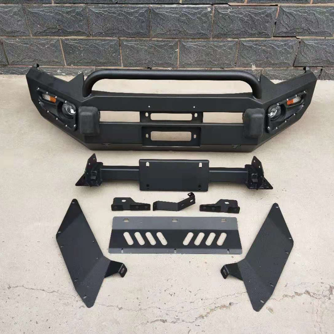 A set of black aftermarket off-road vehicle accessories laid out on a paved surface, including a heavy-duty steel front bumper with a tubular bull bar hoop, integrated light housings, and mounting points. Also visible are various black and gray mounting brackets, a license plate bracket, two large black side/fender protectors, and a gray metal bash plate or skid plate with slotted cutouts.